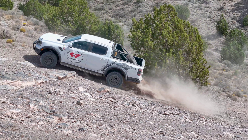 Ford Ranger Raptor bianco che sale su un pendio roccioso a Five Mile Pass, con la polvere dietro le ruote posteriori