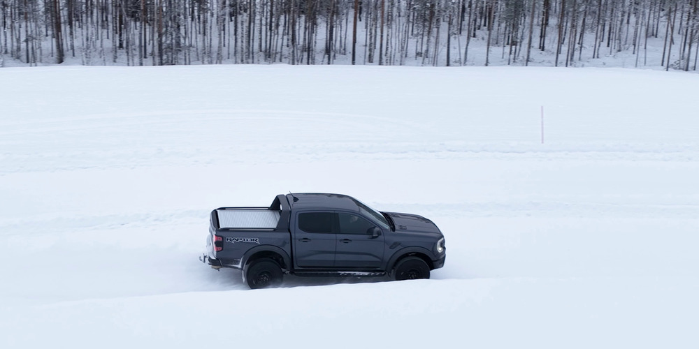 Ford Ranger Raptor grigio che attraversa un percorso di prova innevato accanto a un bosco